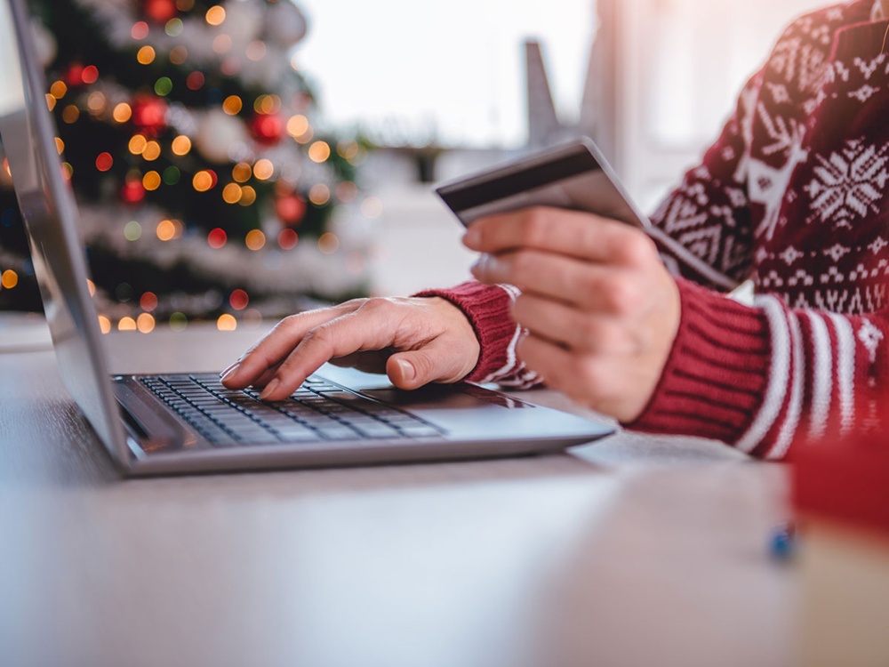 Close-up of a person using a laptop and holding a credit card, with a Christmas tree behind