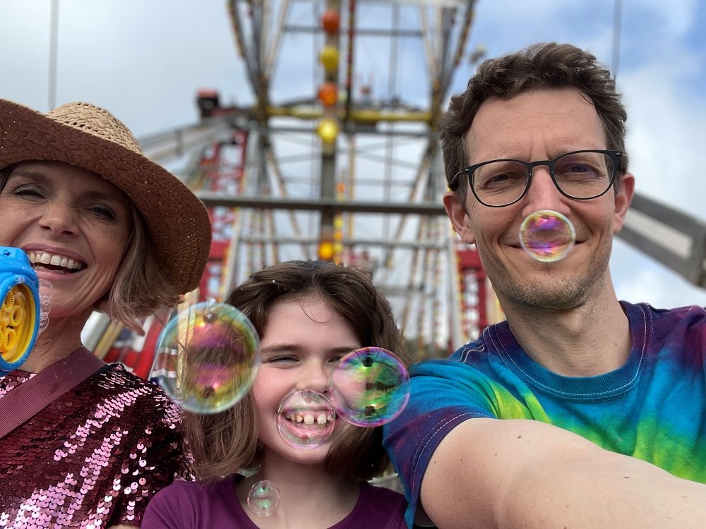 A young mito patient sitting between her parents on a fairground ride blowing bubbles