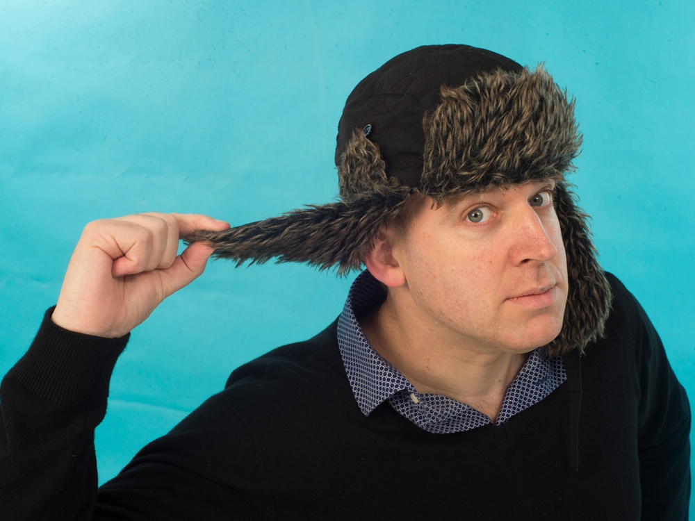 A man in an Ushanka hat holding out one of the ear flaps