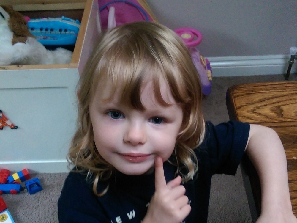 Close-up of a young mito patient with long blonde hair holding her finger to her face