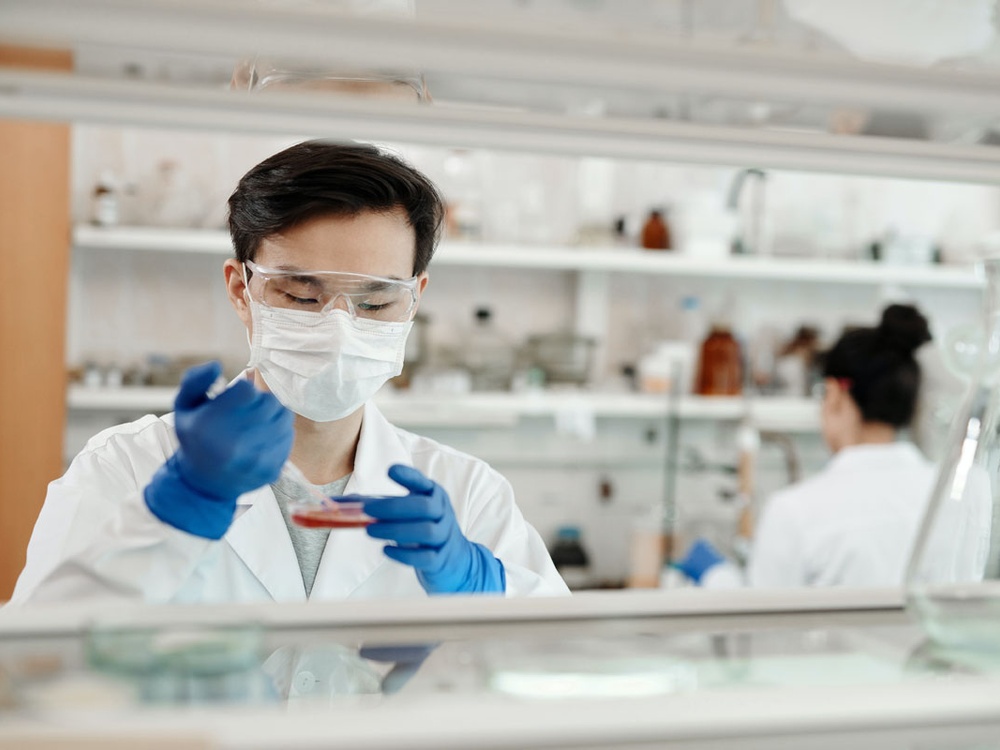 Man in a lab coat, gloves and mask uses a micropipette