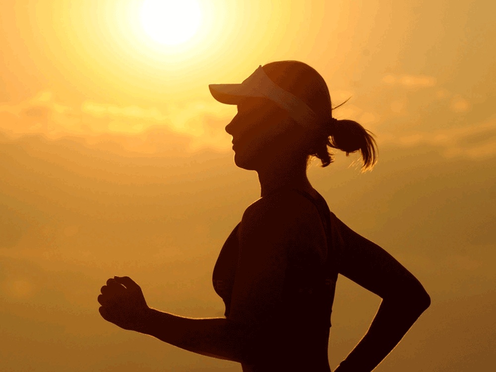 A silhouette of a women running Infront of the sun