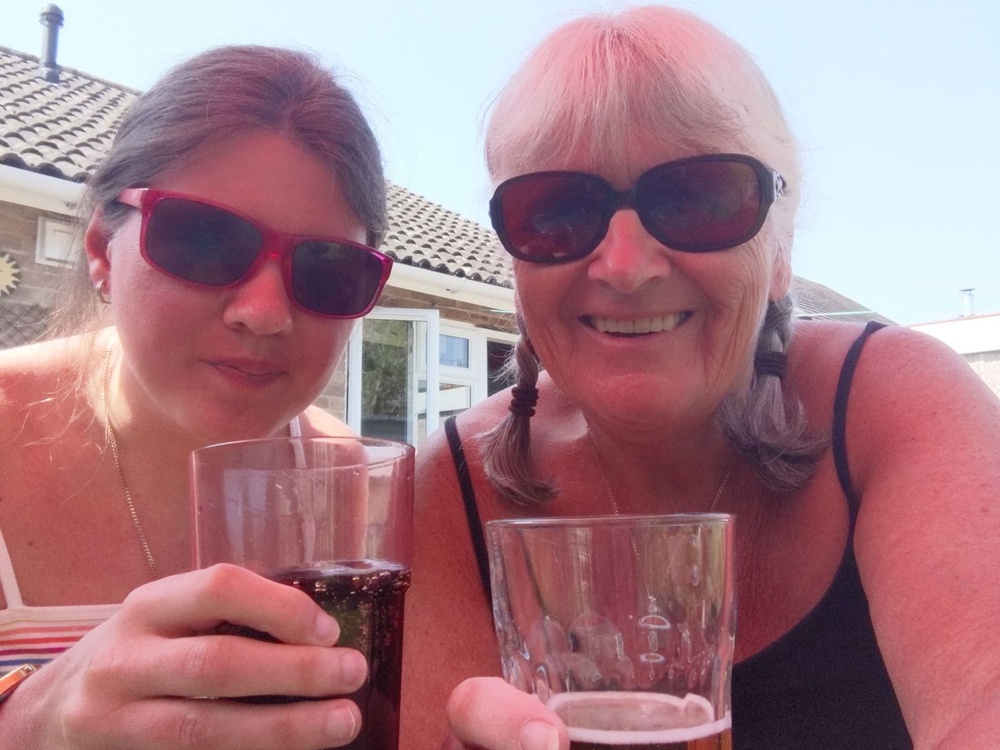 A head shot of two women wearing sunglasses holding drinks up to the camera