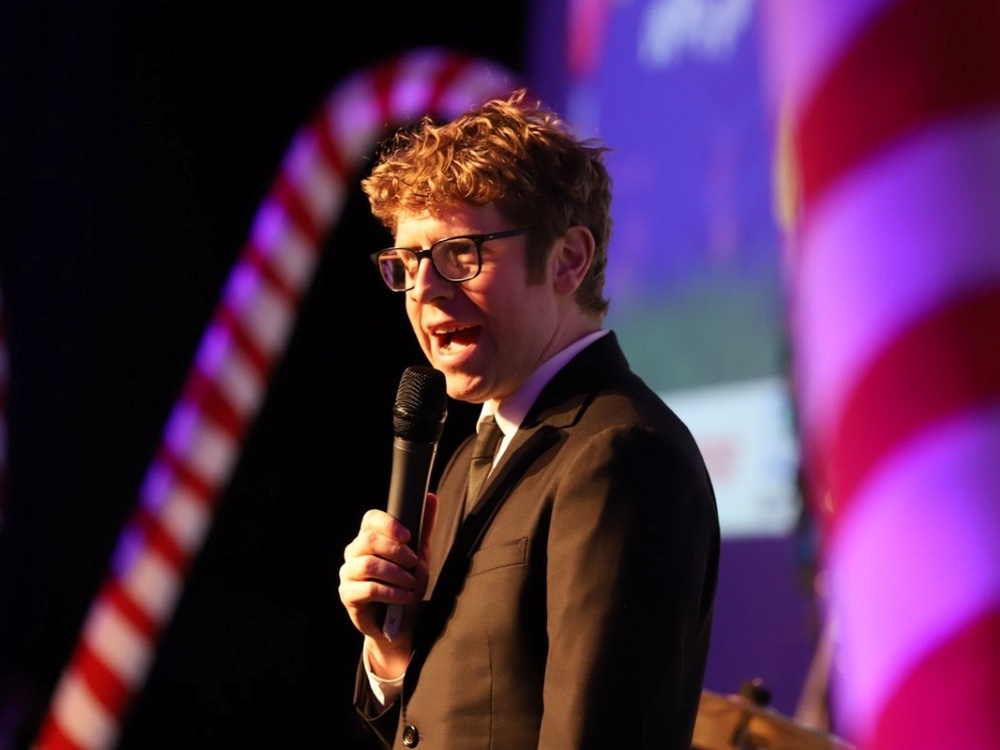 Comedian Josh Widdicombe on stage with a microphone at the Lily Foundation ball