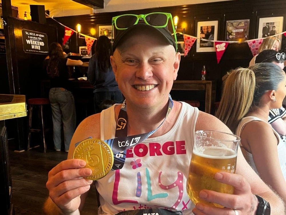 Lily runner George proudly holding his medal and a pint after the London Marathon