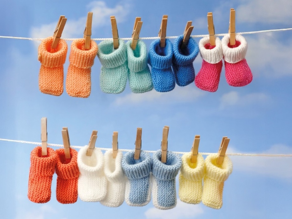 Eight pairs of brightly coloured baby bootees hanging on a clothes line with blue sky behind