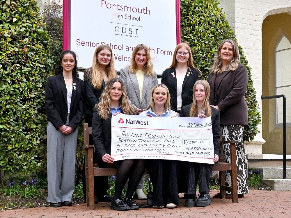 A group of schoolgirls standing together holding a giant cheque for The Lily Foundation