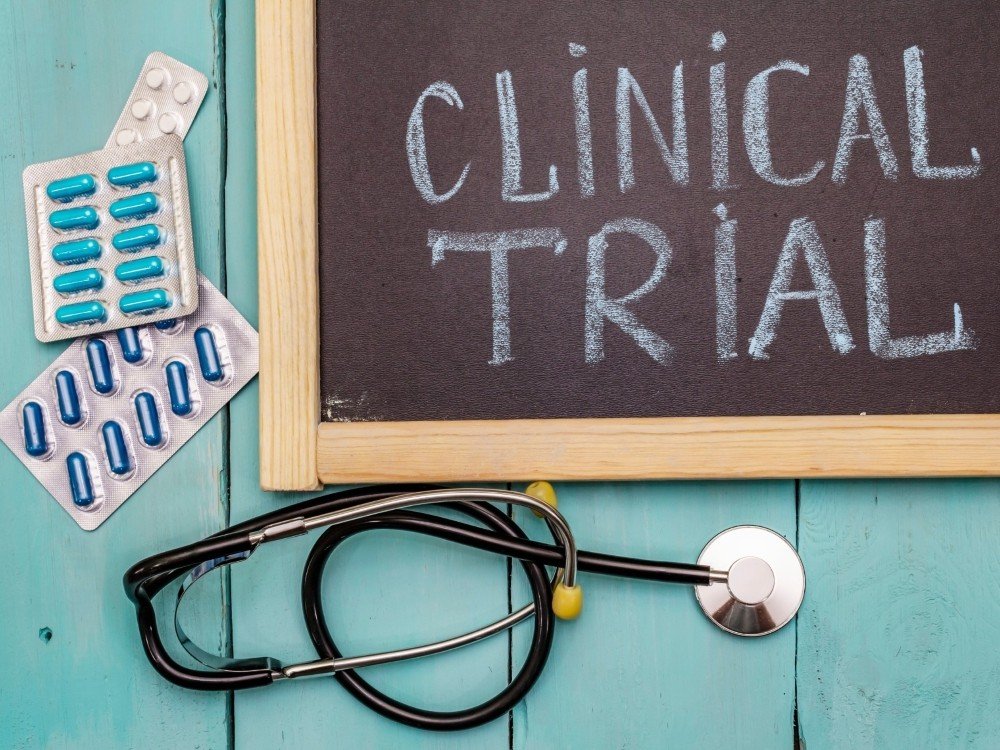 Overhead of a chalkboard with the words 'clinical trial' alongside pills and a stethoscope