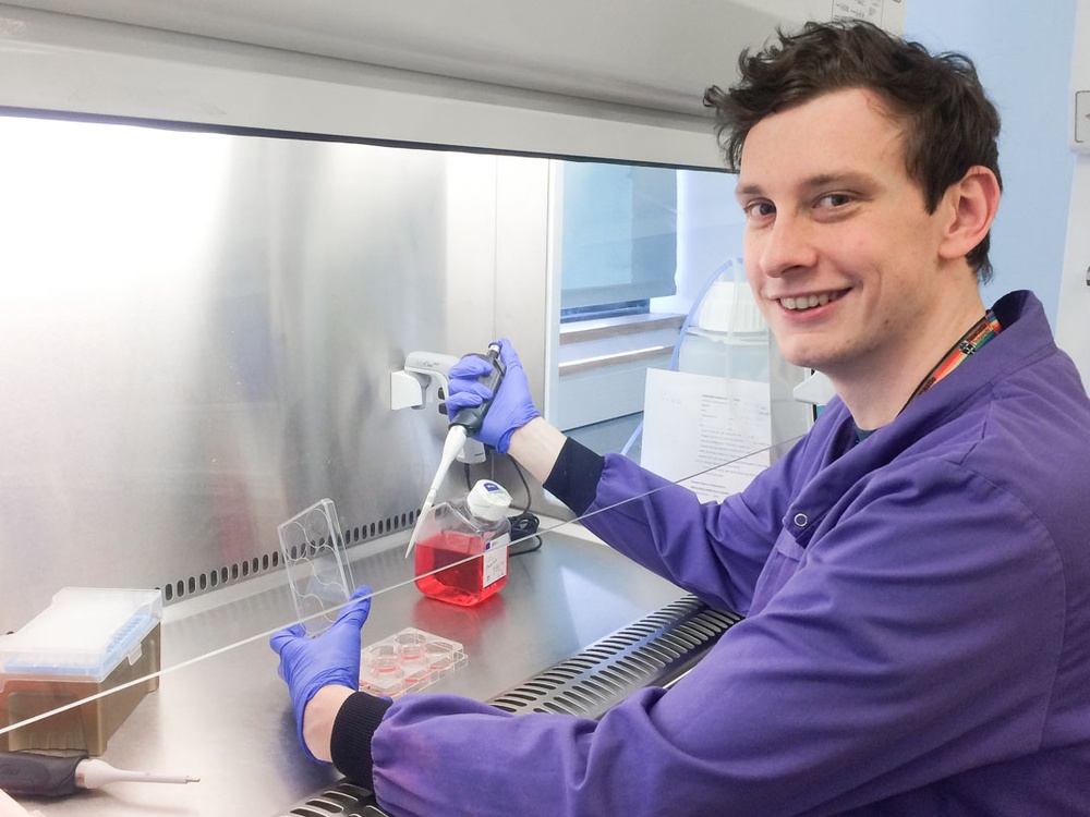 A man in a blue lab coat using a micro pipette