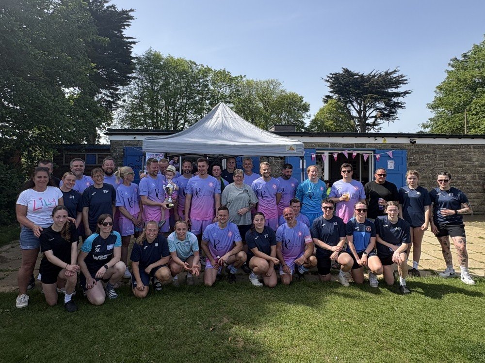 A group of people standing together in the sunshine at a charity football match