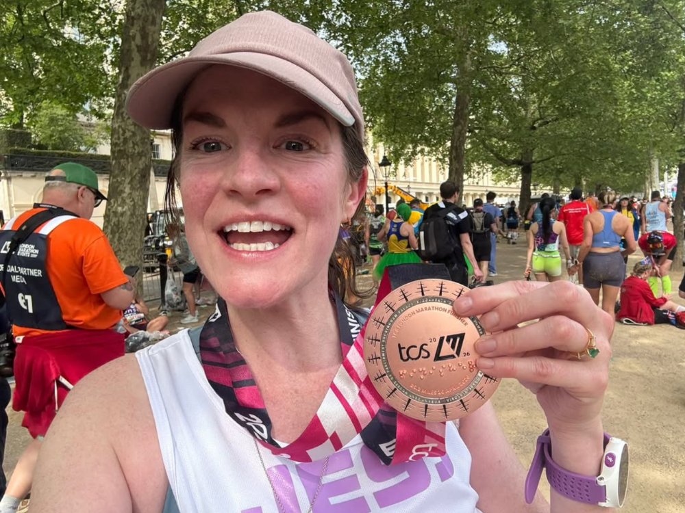 A lady in a baseball cap smiling and holding her London marathon medal up