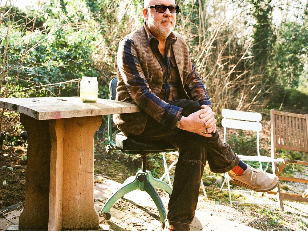 Famous Comedian Jim Moir (Vic Reeves) sitting at a wooden table in a garden