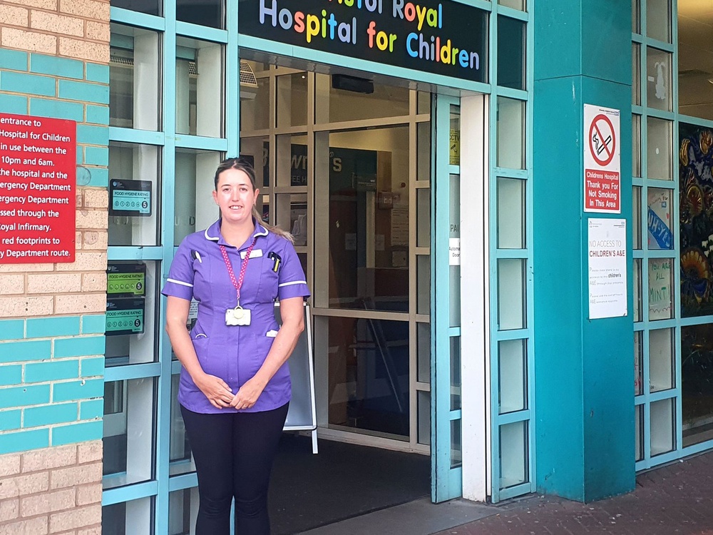 Nurse in a purple outfit, standing in front of a children's hospitalthe