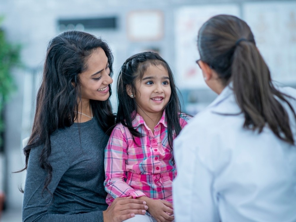 A mother holding her daughter with mitochondrial disease talking to their doctor