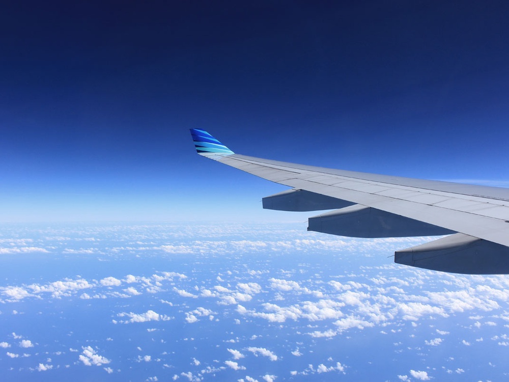 A aeroplane wing with a clear blue sky and clouds behind it