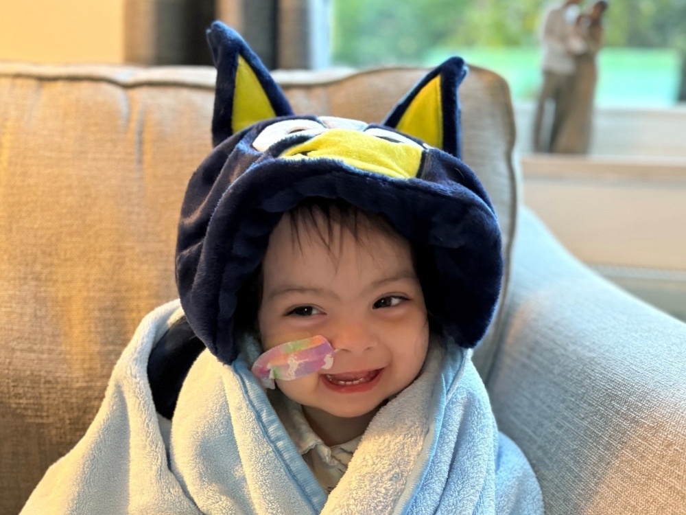 A young mito patient wearing a dressing gown and novelty hat laughing on a sofa