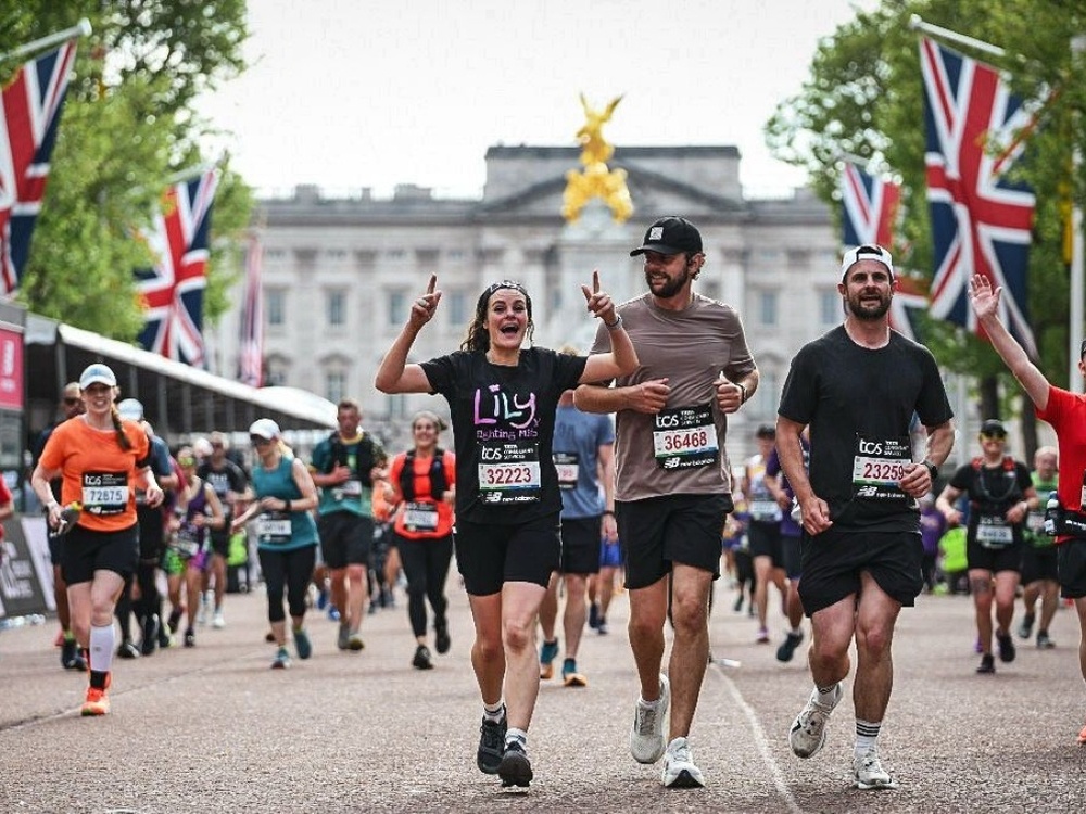 A Lily runner waving and running towards the finish line at the London Marathon