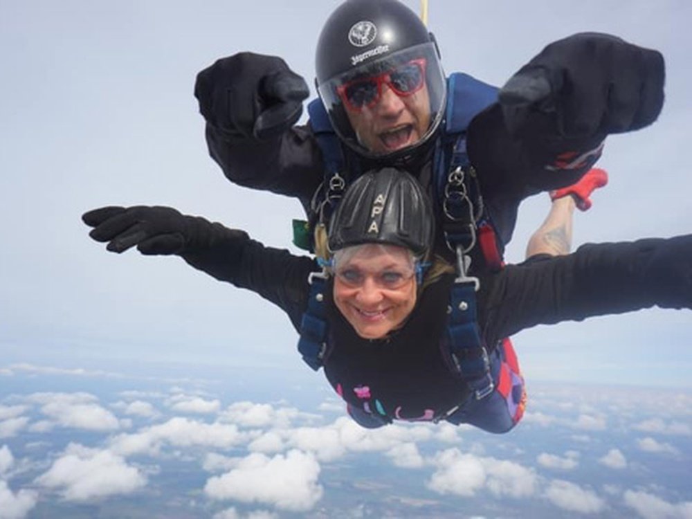 A man and a woman strapped together flying through the sky after their parachute jump