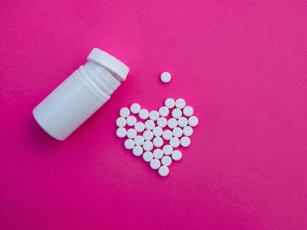Overhead shot of white pills in the shape of a heart lying next to an open pill bottle
