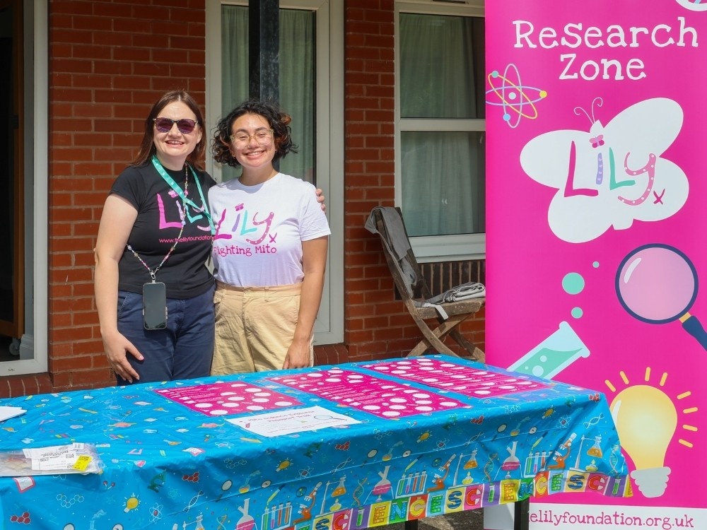 Two ladies in Lily Foundation tops with their arms around each other smiling behind a table