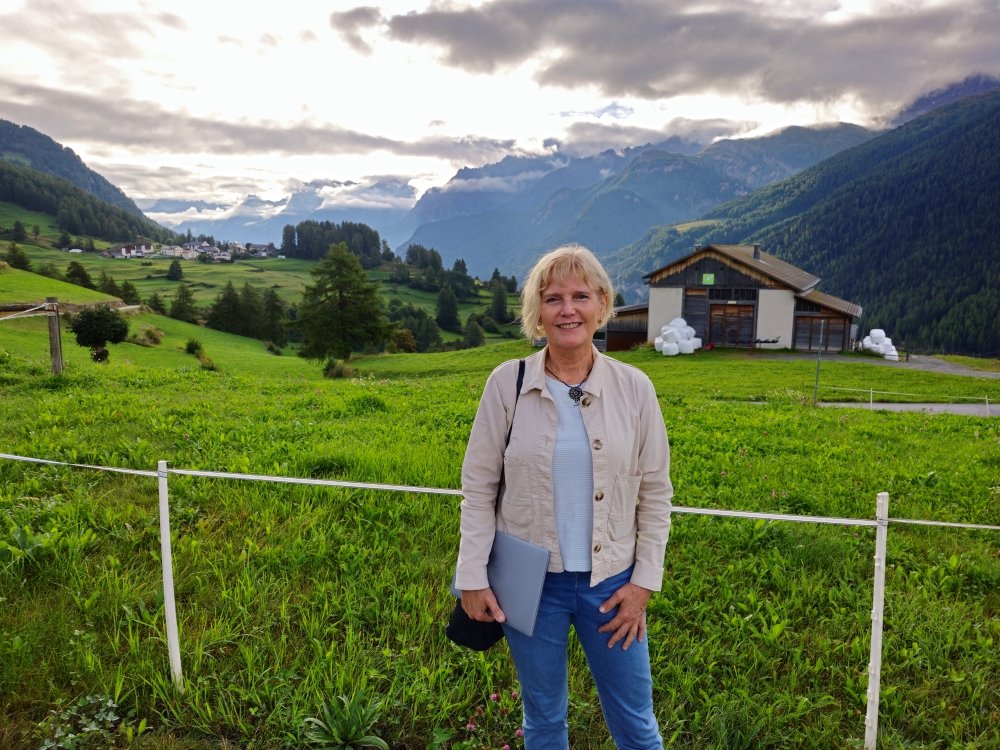 Prof Rita Horvath standing on a lane in front of an alpine meadow view
