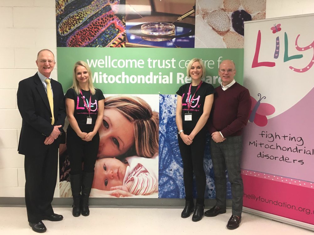 Two members of the Lily Foundation team and two men stand in front of a Welcomme Trust sign