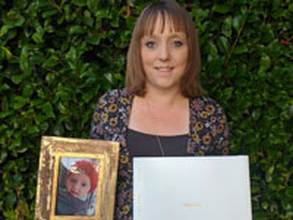 A woman looking into the camera holding a picture of a baby in one and and a book in the other