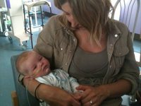 A lady sits in a chair cradling a small baby in a hospital room