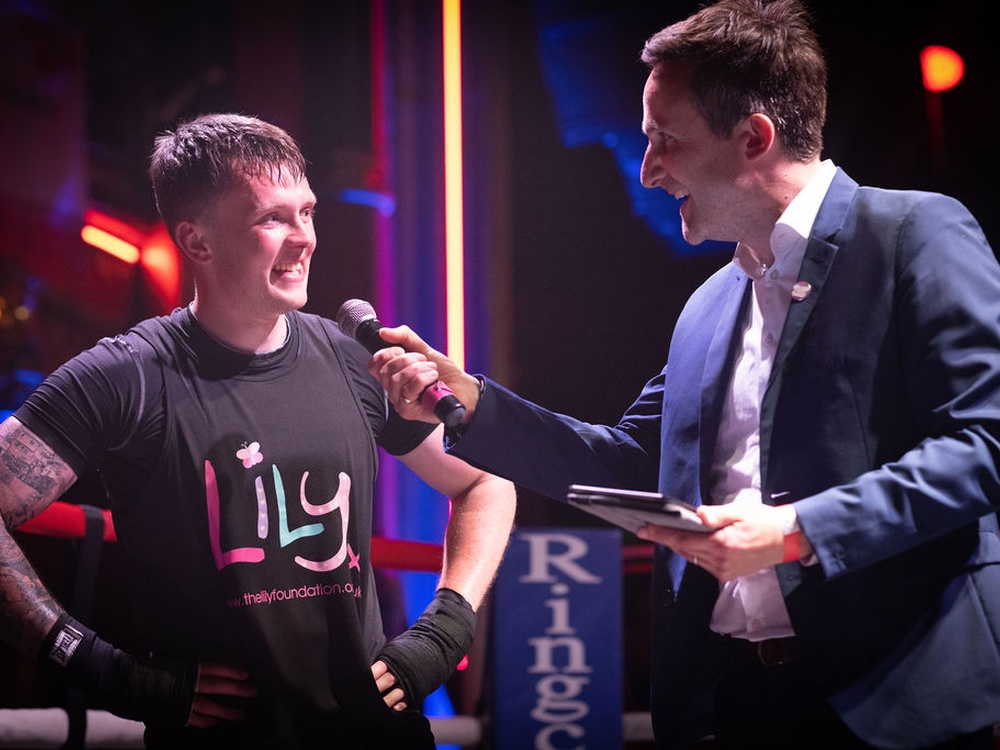 The presenter holds a microphone up at a smiling boxer in a Lily top