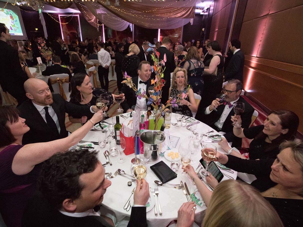 A group of people sitting at a round table raising their glasses in a toast