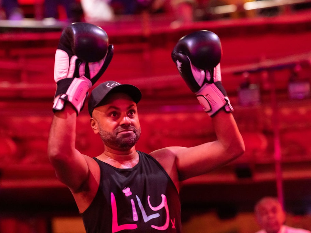 A man in a Lily vest and boxing gloves raises his arms in the air