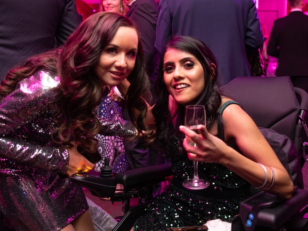 Two young adult mito patients, one in a wheelchair, wearing sparkly dresses