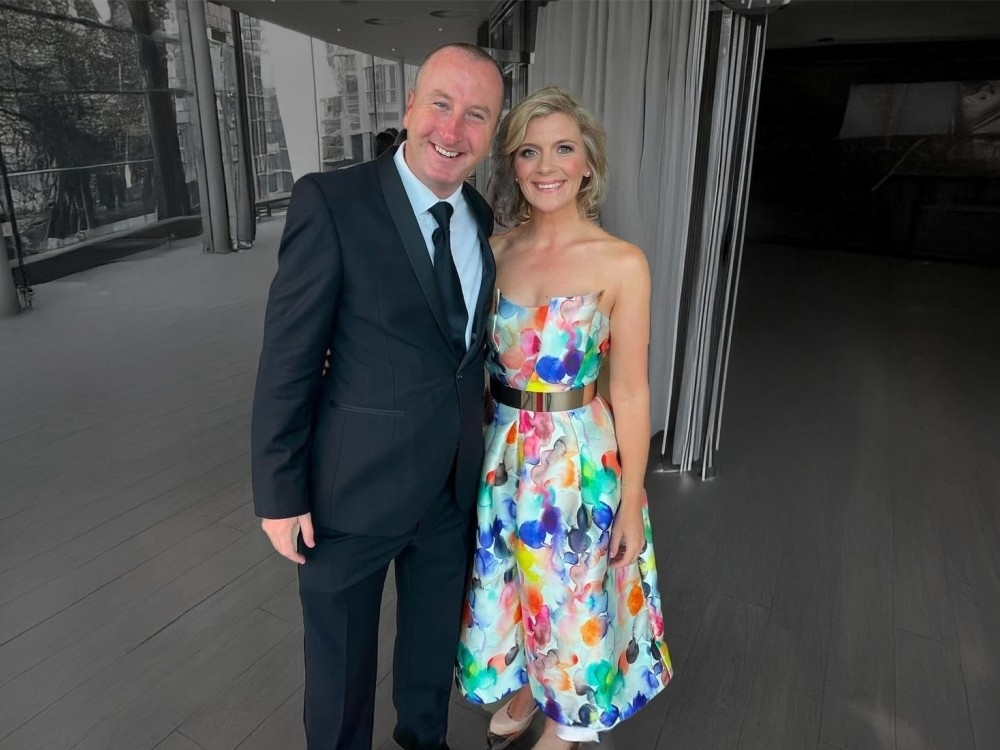 Jane Danson standing in a floral dress outside and event with a man in a black suit