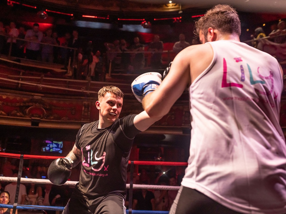 Two male boxers in Lily tops in the ring, one throwing a punch at the other