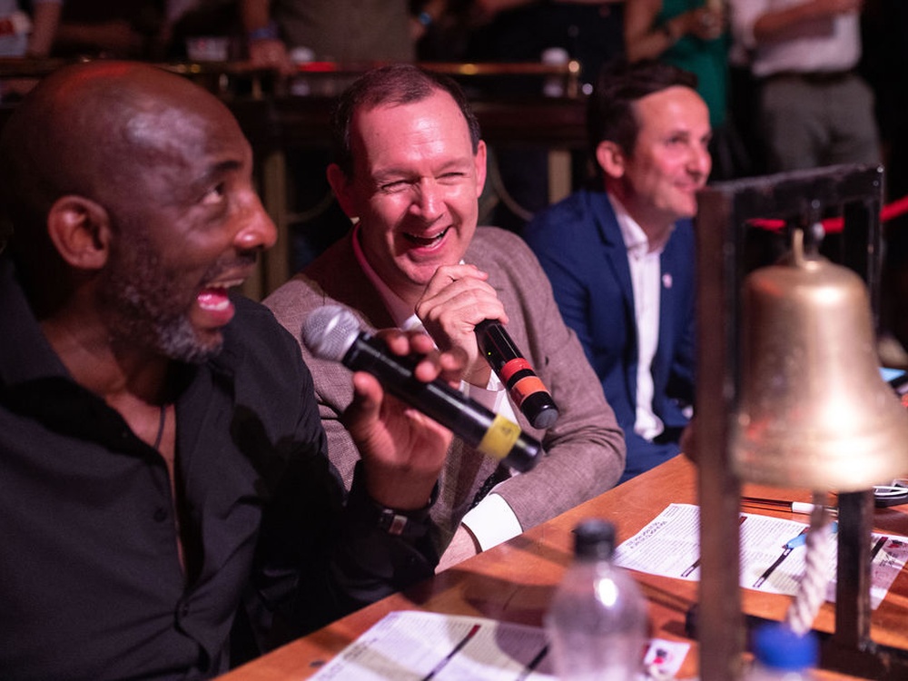 Two men sitting at a desk speaking and laughing into microphones