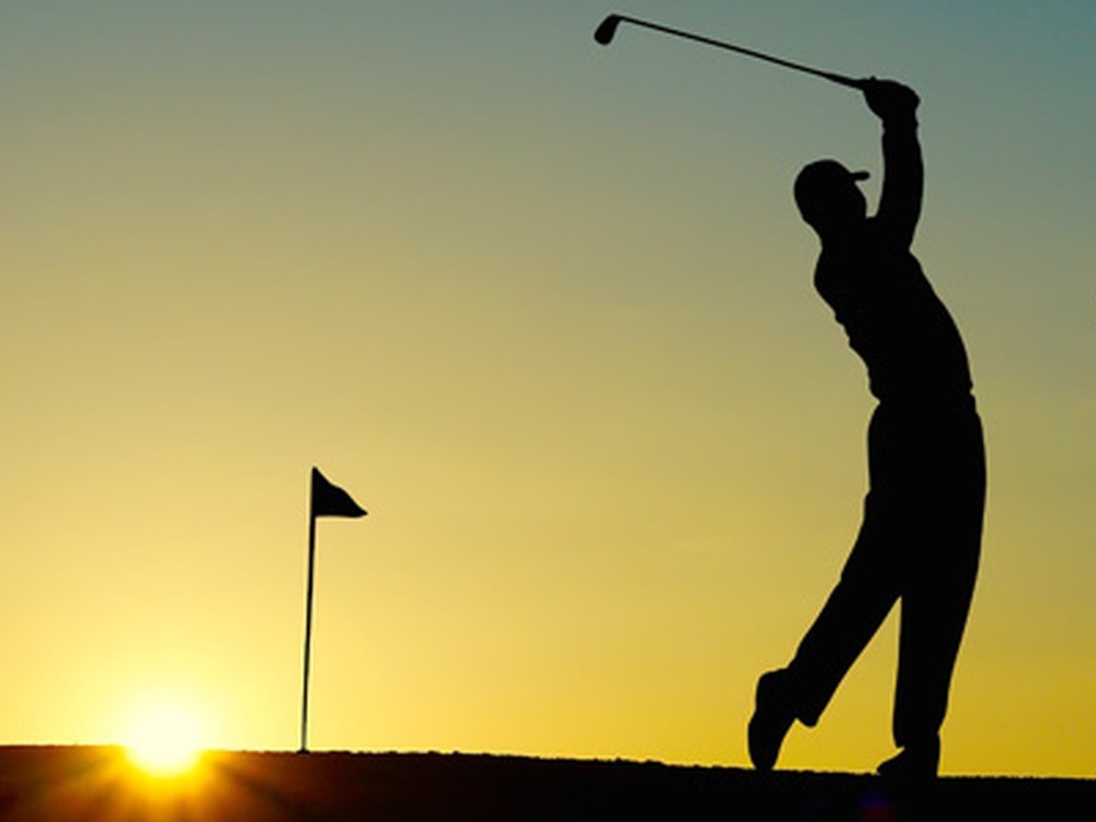 Silhouette of a man swinging a golf club with a sunset behind