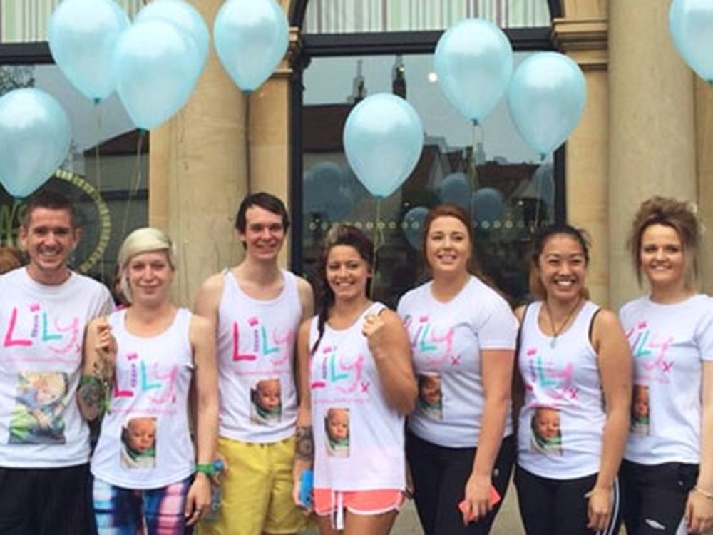 Run with Team Lily and help fight mito! - A group of people lined up in front of a building all wearing white Lily tops and holding pale blue balloons