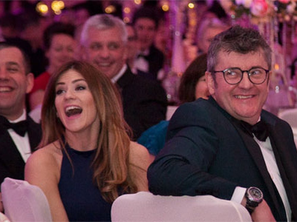 Enjoy the warm glow of a Lily event this winter! - Comedian Joe Pasquale and other guests sitting at tables and laughing at the Lily Foundation charity ball