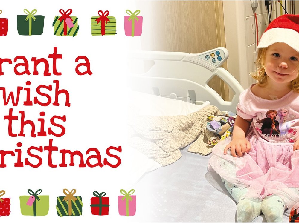 Make someone’s wish come true - A little girl wearing a red Santa hat and sitting on a hospital bed