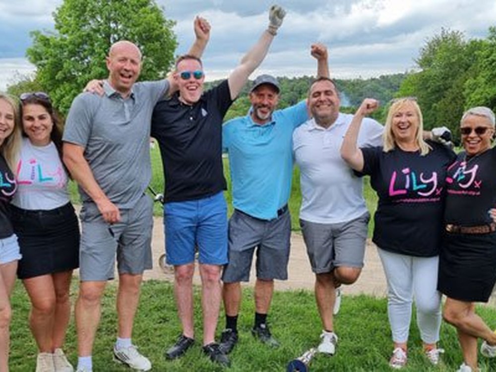 Three cheers for our fun-packed fundraisers! - A group of people on a golf course standing together with their arms in the air smiling