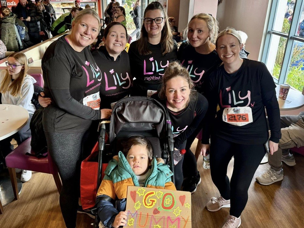 Celebrating our Fundraising Teams - A group of people in Lily tops standing around a child in a buggy holding a sign saying 'Go Mummy'