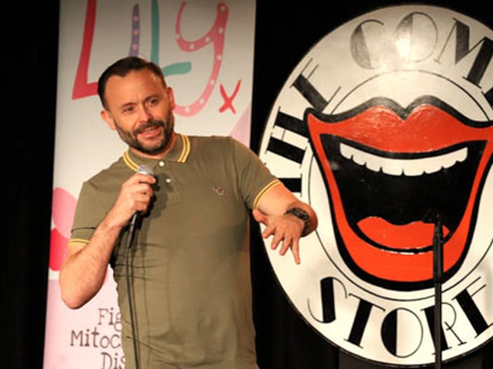 Lily Comedy Night is back! - Comedian Geoff Norcott standing in front of the Comedy Store logo holding a microphone at the Lily comedy night
