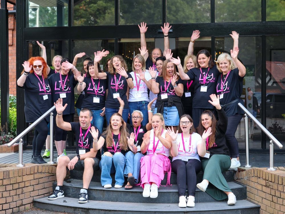 Celebrating 15 years of… The Lily Foundation! - A group of Lily Foundation staff and volunteers sitting and standing on the steps of a hotel entrance waving and smiling