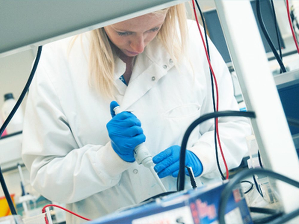 ILAP to smooth approval process for rare disease drugs - A lady in a science lab wearing a white lab coat and blue protective gloves focusing on scientific equipment