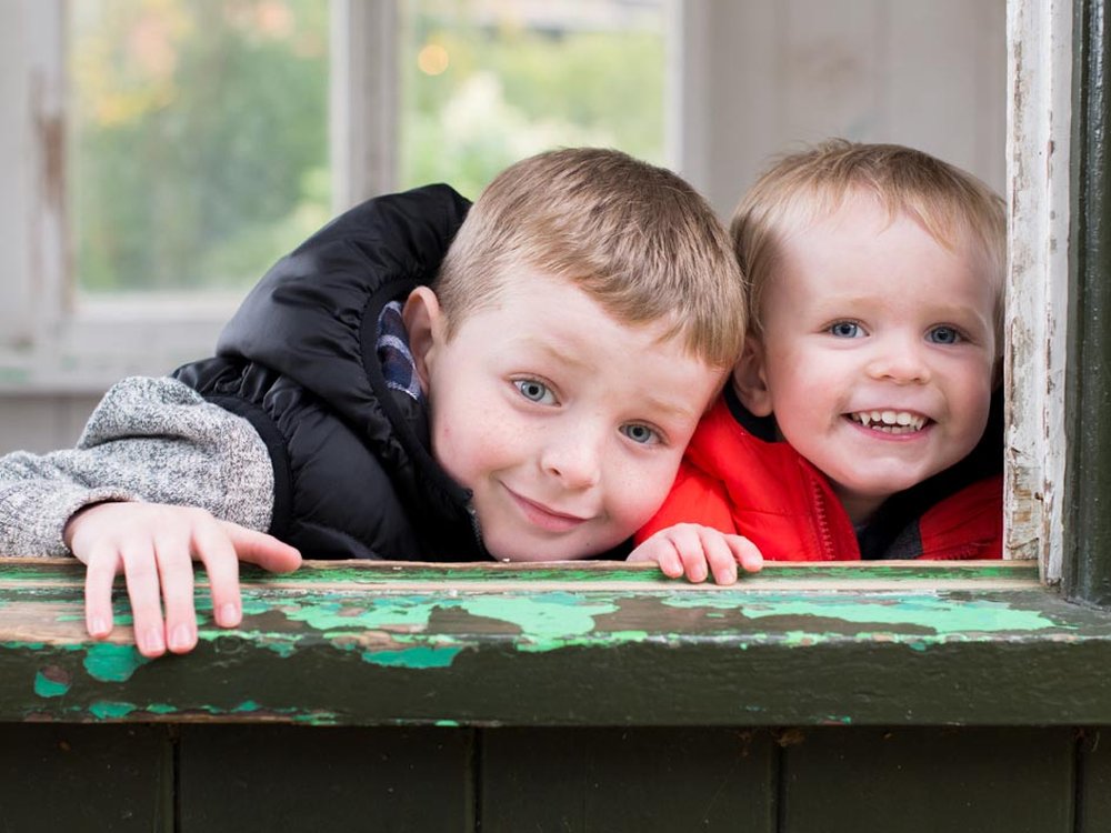 Seizure drug for mito patients begins clinical trials in UK - Two young children smiling and peering through a window with a well-worn wooden frame