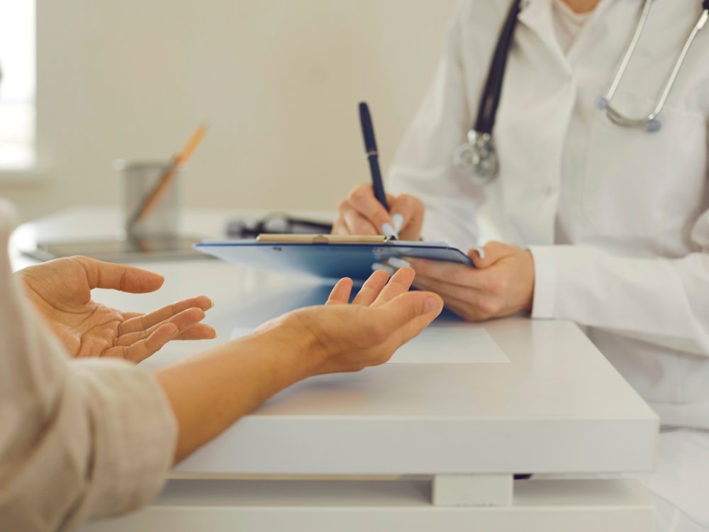 Close-up of clinician in a white coat with a clipboard and a patient's hands