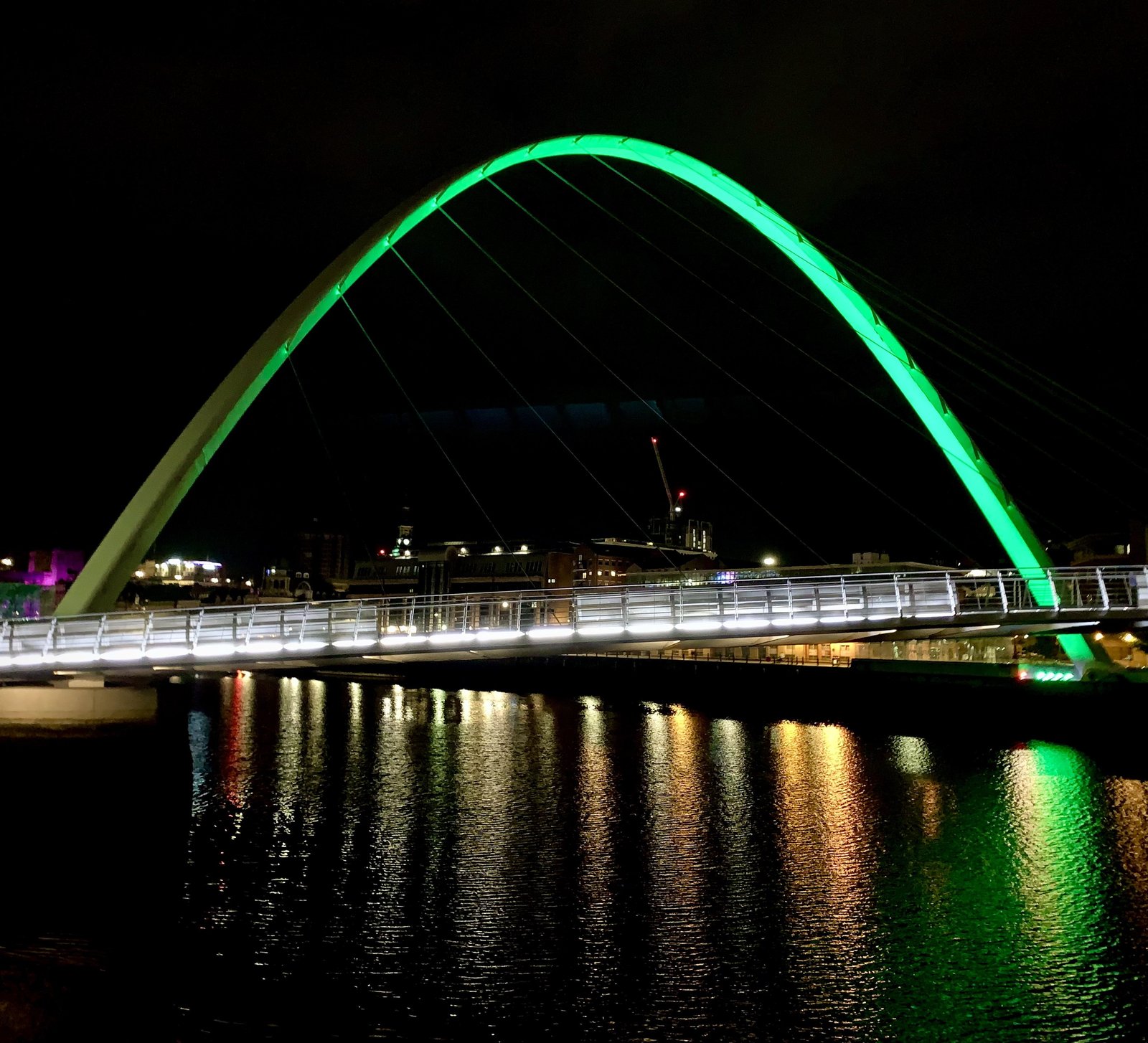 The Gateshead Millennium Bridge lit up green in the darkness
