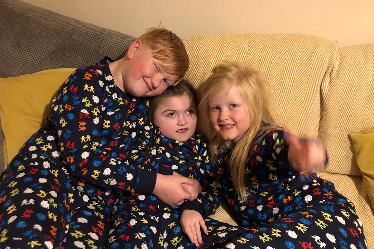 three children in matching Pj's sit of a sofa