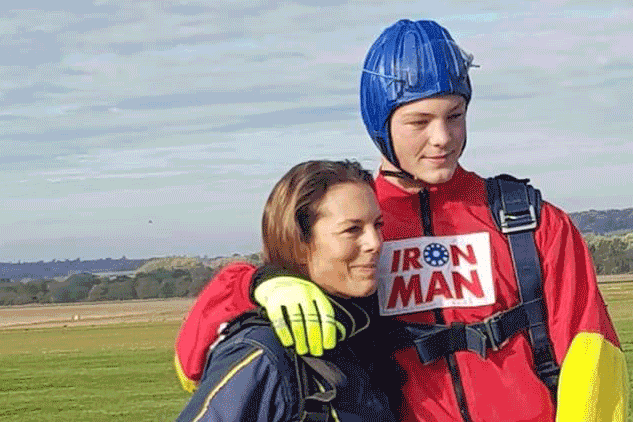 A man in a skydiving outfit stands next to a lady in a field