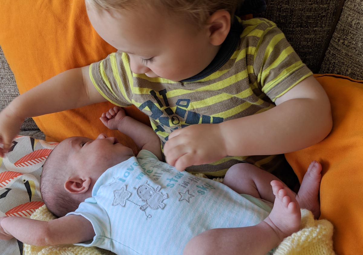 A toddler looks down at a little baby lying on its lap